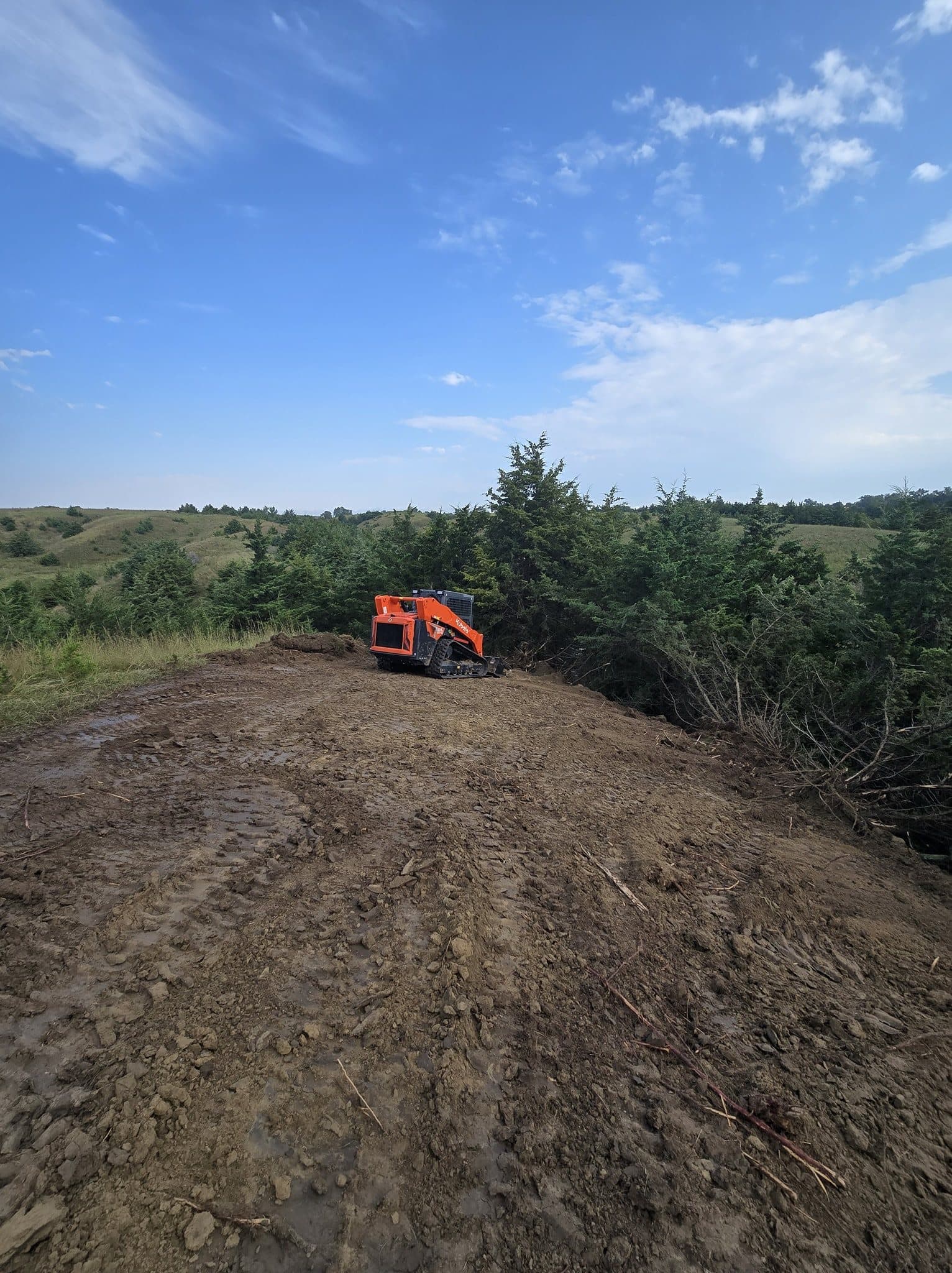 Skid steer clearing brush and moving dirt on a Nebraska hilltop.