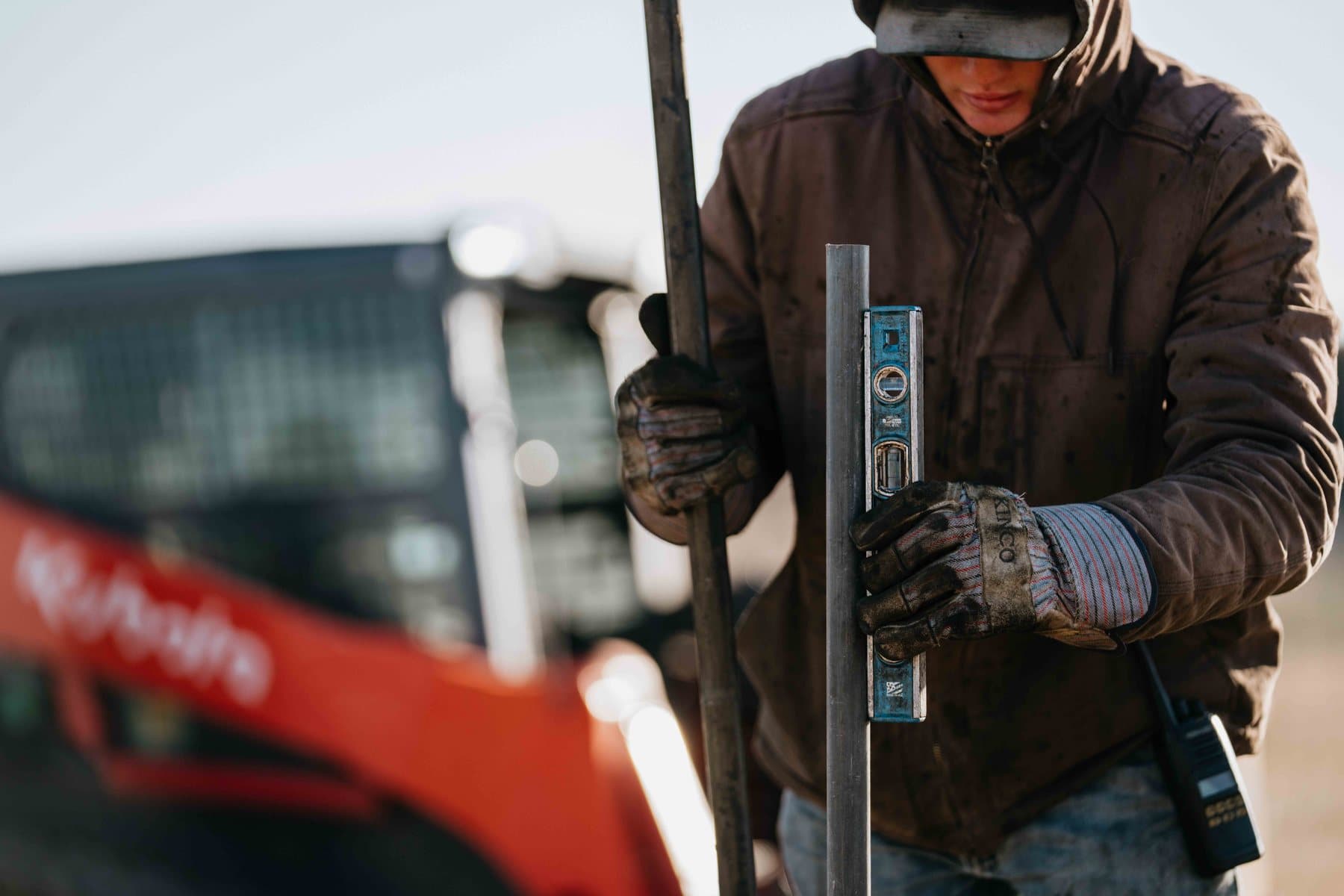 Crew member leveling a steel post with a skid steer working behind.